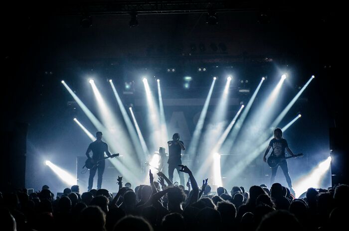 Concert scene with band performing on stage, bright lights shining, and audience enjoying the music experience.