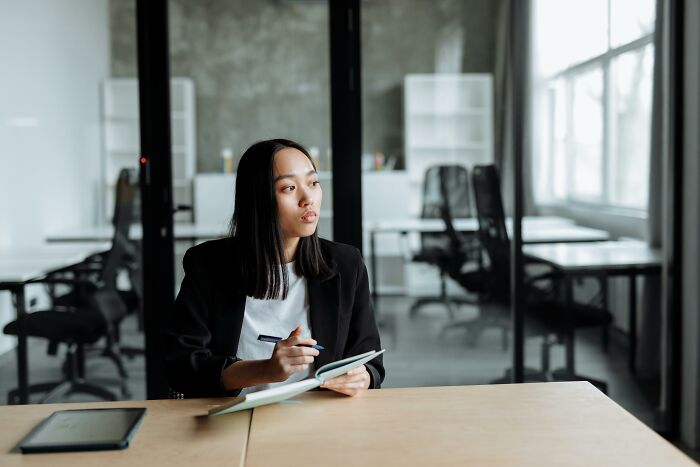 Person in a modern office pondering ways to save money and find more fulfillment in 2025, with a tablet and pen.