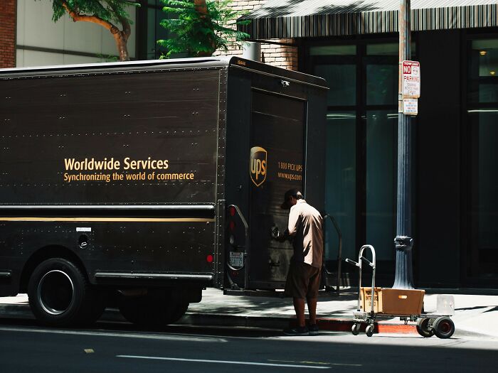 "UPS truck parked on street, delivery person handles packages; scene of a job exit."