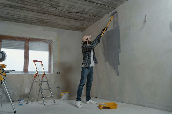 Person using a paint roller to cover a wall, demonstrating an unconventional painting technique.