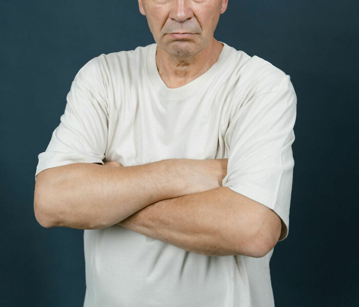 Man in a white shirt with arms crossed, representing social norms that need reevaluation.