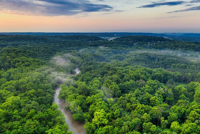 Aerial view of lush, green forest in the Tuscany region, Italy, under a colorful sunset sky.