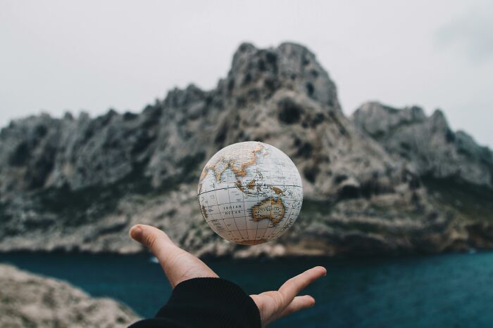 Hand holding a globe in front of a rugged mountain landscape, symbolizing key world moments in history.