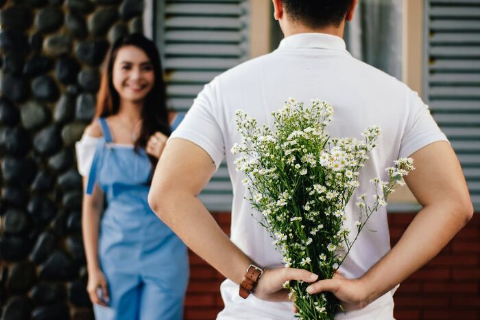 Man holding flowers behind his back, surprising woman, showcasing non-sexual gestures that attract women.