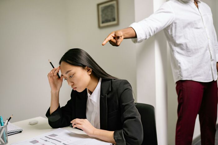 Woman at a desk looking stressed, with a person pointing behind her, illustrating socializing and driving concerns for older adults.