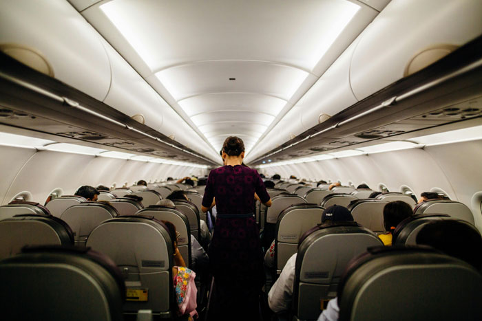 Airplane interior with passengers seated, flight attendant walking down the aisle.