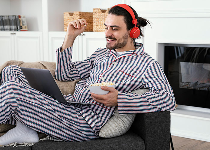 Man in striped pajamas with red headphones watching laptop, symbolizing post-brain rot era relaxation at home.