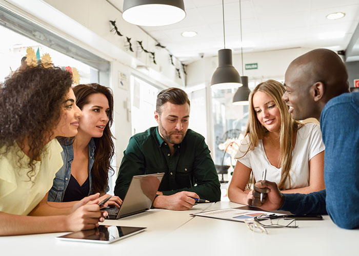 Group discussing post-brain rot era, seated around a table in a modern office, with laptops and documents.