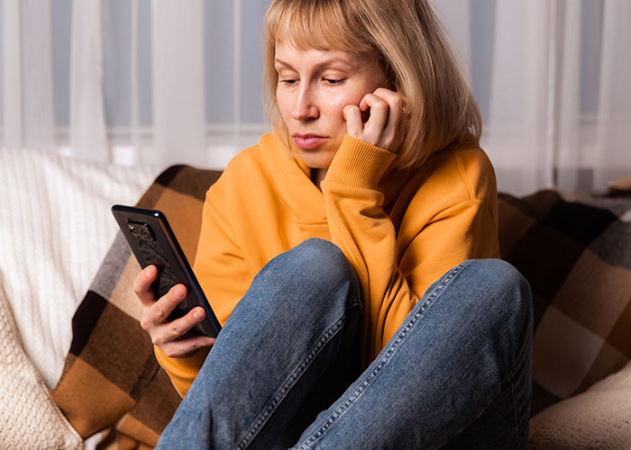 Person in yellow hoodie using smartphone, pondering post-brain rot era at home.