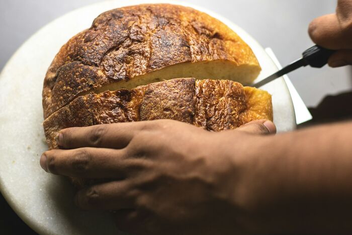 Hands slicing homemade bread on a cutting board.