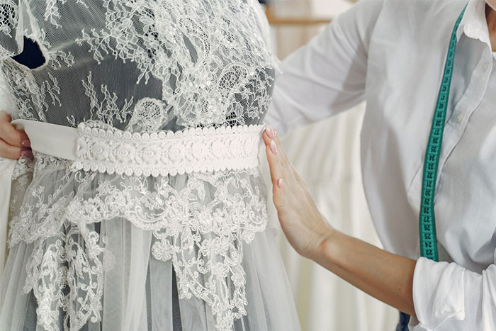 Bridal shop owner adjusting lace on a wedding dress, illustrating a family feud over a second dress request.