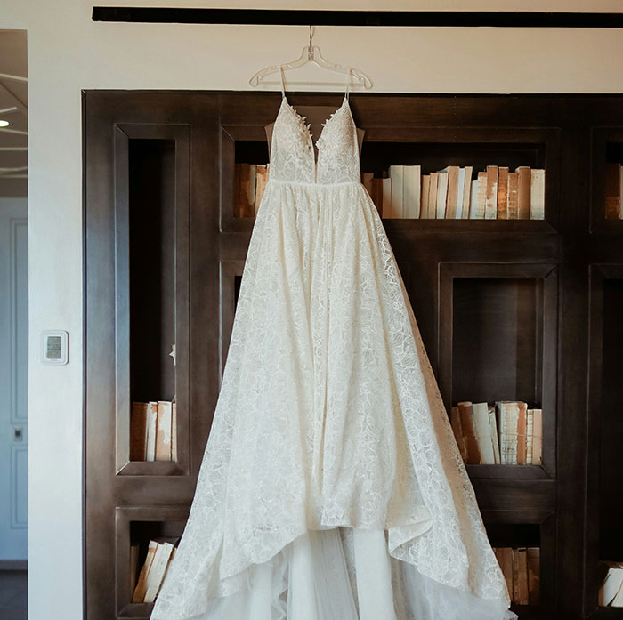 A lace wedding dress hanging in a bridal shop against a bookshelf backdrop.