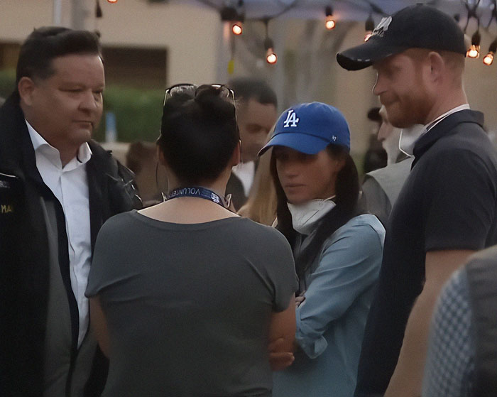 People gathered at an outdoor event, including individuals in baseball caps and causal attire, conversing in a social setting.