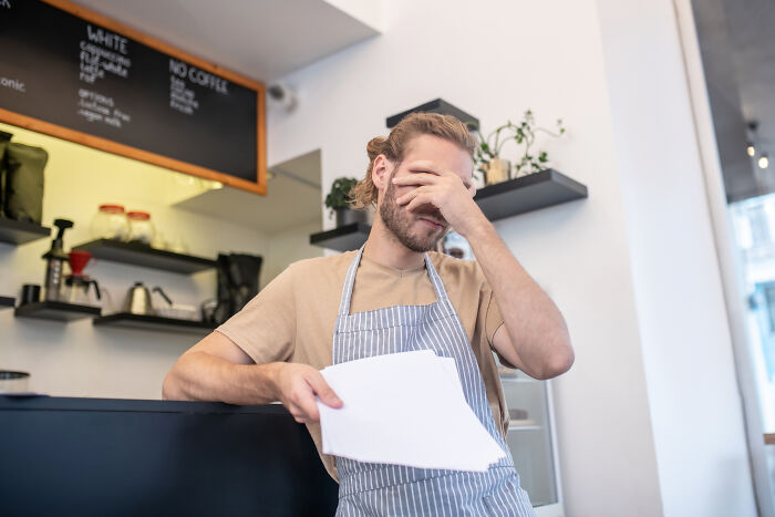 Barista holding papers, looking frustrated during a job exit in a cafe setting.