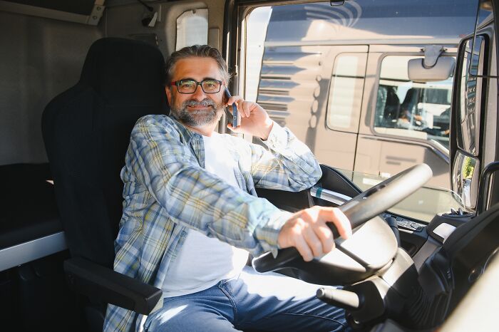 Man in a plaid shirt and glasses smiling while sitting in a truck, possibly quitting job in a revengeful way.