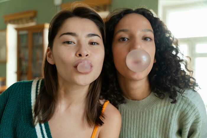 Two women blowing bubbles with gum, demonstrating psychological tricks in a playful setting.