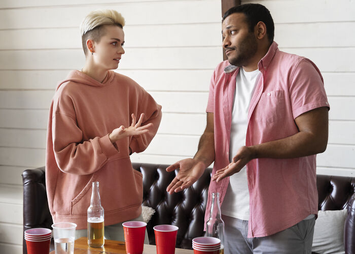 Two people engaged in a conversation, possibly using psychological tricks, surrounded by red cups and bottles.