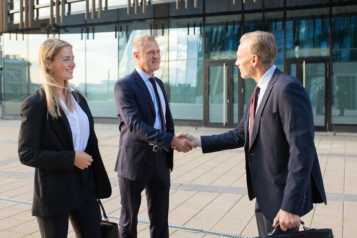 Business professionals shaking hands outside an office building, demonstrating psychological tricks in interactions.