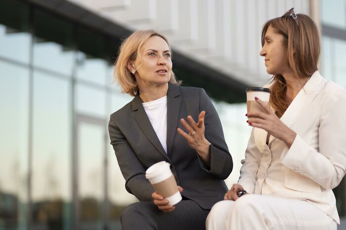 Two women in conversation, both holding coffee cups, illustrating psychological tricks in social interactions.