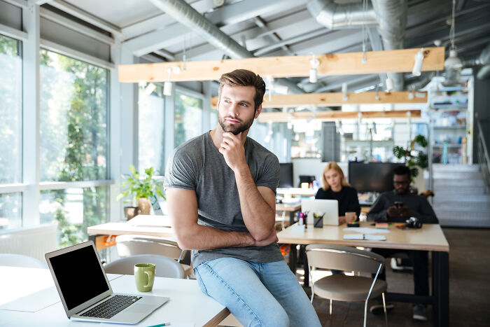 Man in casual attire sits thoughtfully in a modern office, suggesting psychological tricks in workplace environments.