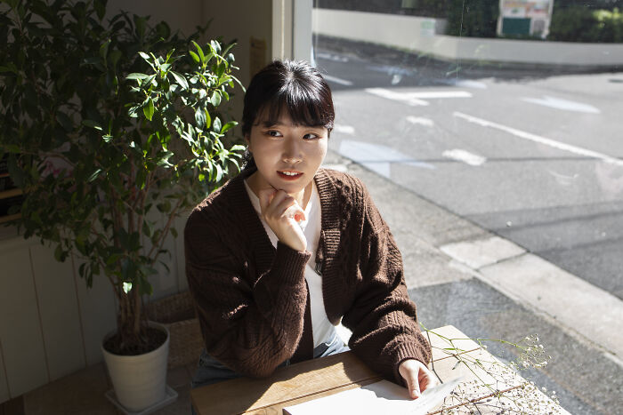 A woman sitting at a table by a window, appearing thoughtful, in a cozy café setting, demonstrating psychological tricks.