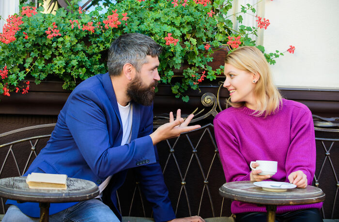 A man and woman engage in a lively conversation at a cafe, illustrating interesting psychological tricks in social interactions.