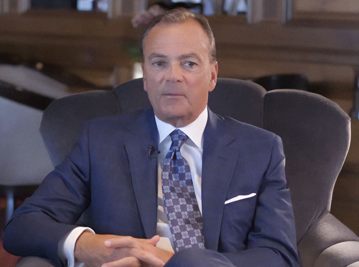 Man in a suit sitting in an armchair, discussing private firefighters protecting homes from wildfires.