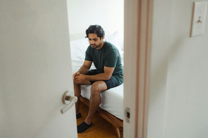 Man sitting on a bed looking thoughtful, related to engagement and proposal.