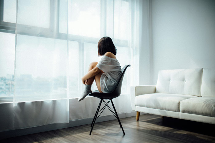 Person sitting on a chair by the window, reflecting on a ring proposal and anniversary engagement moment.