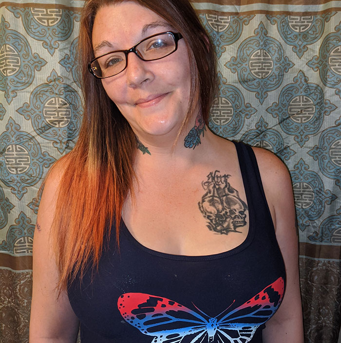 Woman with glasses and tattoos wearing a black tank top with a butterfly design.