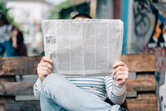 Person sitting on a bench, holding a newspaper, representing job exits and quitting stories.