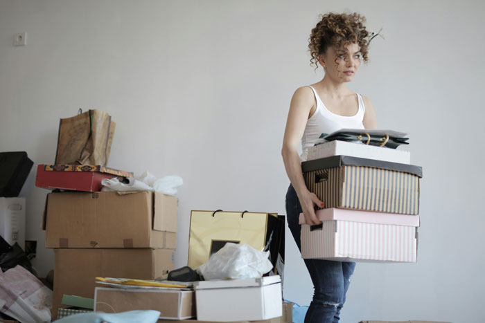 Person holding boxes in a cluttered room, surrounded by cardboard and disorder, suggesting a messy situation.