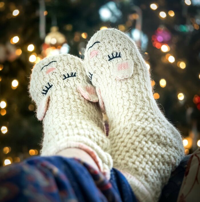 Cozy knitted slippers with sheep faces, an expensive item worth the investment, in front of a holiday-lit background.