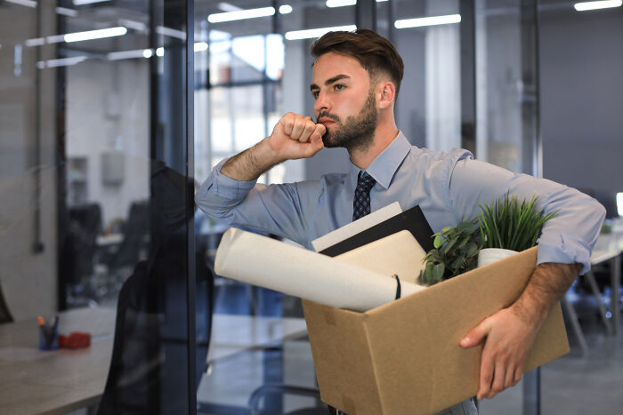 Man carrying a box of belongings, symbolizing a savage and revengeful job exit in an office setting.