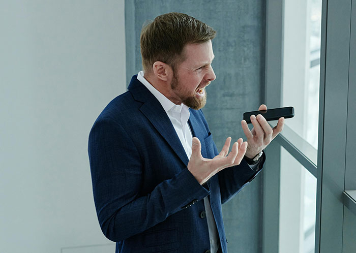 Man in a suit angrily talking on phone, expressing frustration in a modern office.