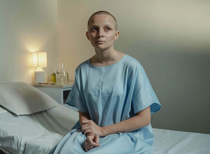 Person in a blue gown sitting on a bed, looking contemplative in a softly lit room, showcasing an introspective mood.