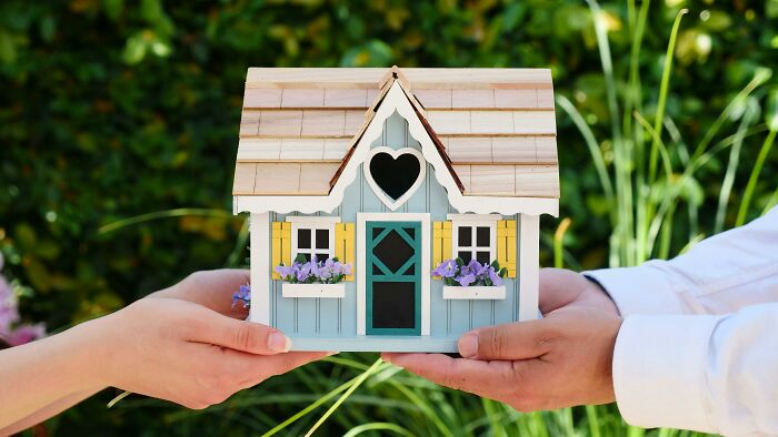 Two hands holding a model house, symbolizing ways to protect your home title from scammers.