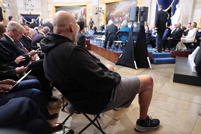 Senator in gym shorts attending a formal presidential inauguration event, seated in a crowded venue.