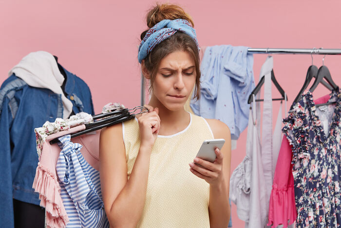 Woman in clothing store, holding clothes and checking her phone.