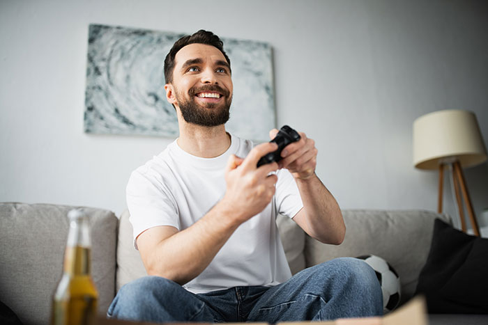 Man playing video games on a couch with a drink nearby, related to family rent dynamics discussion.