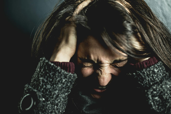 A frustrated woman holding her head, expressing anger in a dimly lit setting.