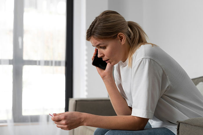 Woman talking on phone, seated indoors, looking concerned.