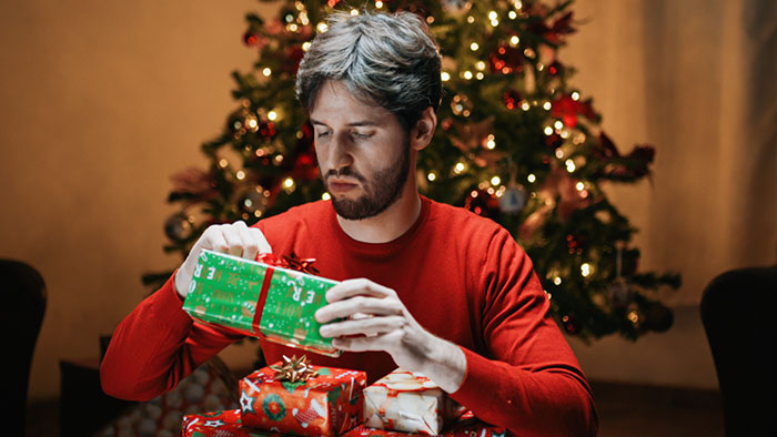 Man in red shirt wrapping gifts near Christmas tree.