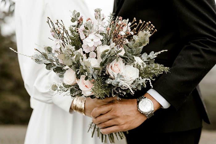 Bride and groom holding a bouquet, showcasing wedding color scheme with white and greenery.