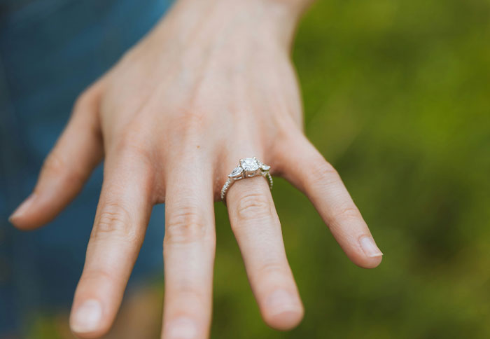 Close-up of a hand wearing a diamond ring, set against a green background, highlighting the keyword "real baby".