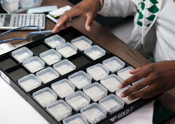 Person sorting small containers, possibly with beads, on a table with a calculator nearby.