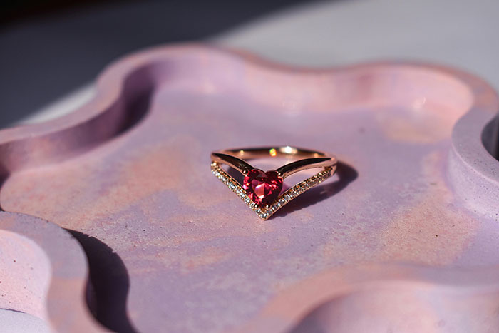 Heirloom ring with a heart-shaped red gemstone on a decorative pink tray.