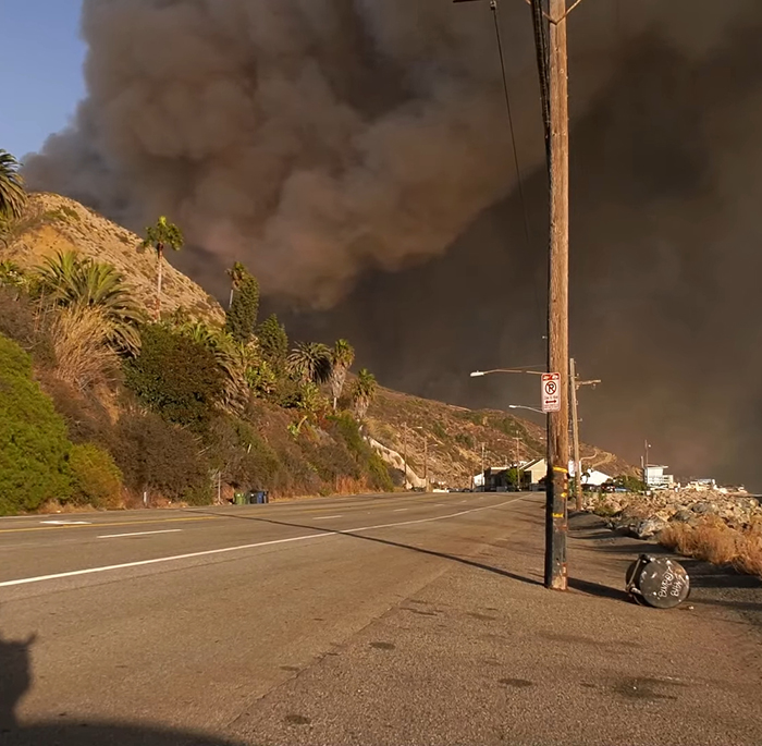 Road with thick smoke from LA wildfires, highlighting impact as celebrities face criticism.