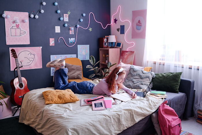 Child relaxing in a colorful family home bedroom, reading a book with wall art and a guitar nearby.