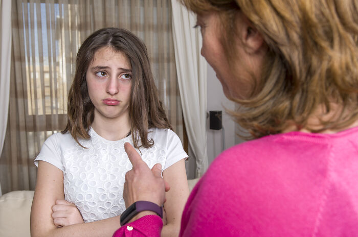 A woman in a pink sweater discussing squatters rights with a young girl wearing a white top in a family home.